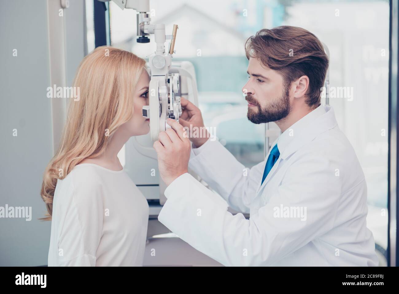 Health care, medicine, eye sight and technology concept. Side profile photo of brunet bearded optician checking blond`s lady patient intraocular press Stock Photo